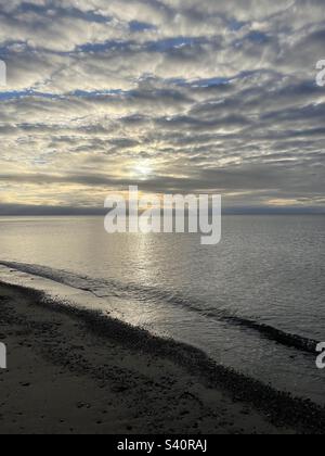 Sun rays shining through layers of clouds. Atlantic Ocean and the beach. Waves lapping on the beach. Stock Photo