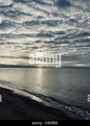 Sun rays shining through layers of clouds. Atlantic Ocean and the beach. Waves lapping on the beach. Stock Photo