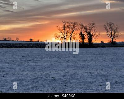 Sunrise across snow covered wintery field Stock Photo