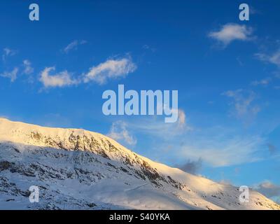 Wispy clouds in a blue sky over the snowy French Alps. Stock Photo