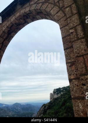 Looking through the arch on the outer wall of the Santa Maria de Montserrat Abbey in Spain’s Catalan lowlands. The Catholic Abbey is known for its choir and mountainous location Stock Photo