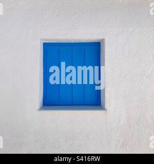 Traditional blue shuttered window on white wall in Greece Stock Photo