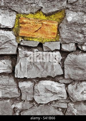 A lone “color select” stone, with some mossy soil stand out in this rough hewn stone wall. Stock Photo