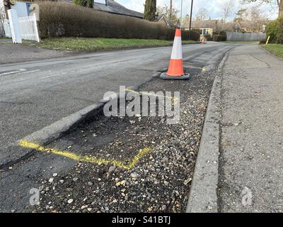 Damaged road with large pot holes marked by traffic cones Stock Photo