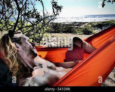 A man relaxes in an orange hammock overlooking the beach in Nosara Costa Rica Stock Photo