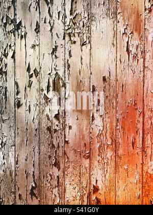 Full frame texture background of flaky and peeling paint on a wooden surface with the orange glow from the heat of a fire and copy space Stock Photo