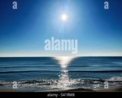 Sun reflections on the sea as the waves ripple and lap on the beach. Horizon and shimmering light. Mediterranean. Stock Photo