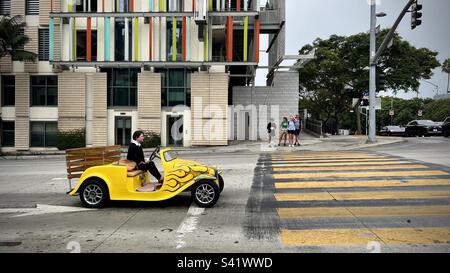 SANTA MONICA, CA, AUG 2022: woman driving a distinctive, bright yellow, custom car, stopped at yellow crosswalk next to modern apartment building Stock Photo