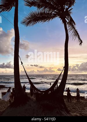 Sunset / sunrise above the ocean, people watching the sunset and a hammock tied to two palm trees. Tulum, Mexico Stock Photo