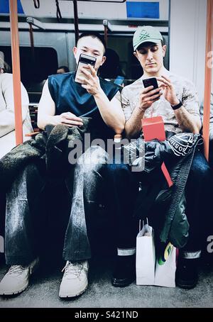 Two men looking at their phones on the underground in London UK Stock Photo