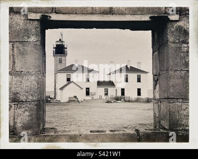 Black and white photo with Hipstamatic filter of Beavertail Lighthouse in Jamestown, Rhode Island, USA. Lighthouse is framed by window in an abandoned building. Stock Photo