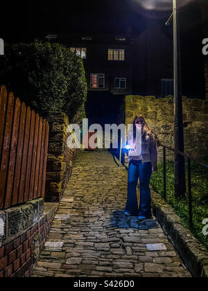 Teenager on cobbled path at night holding iphone with flashlight Stock Photo