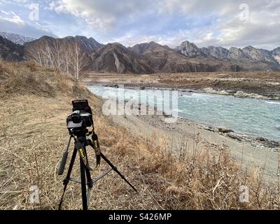 Nikon D750 camera with square light filters stands on the edge of the river bank with mountains in Altai. Stock Photo