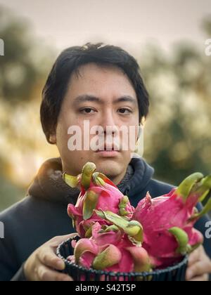 Young man holding basket of dragon fruits against setting sun. Stock Photo