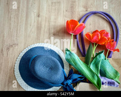 flat lay of orange tulips on straw bag next to straw hat. Stock Photo