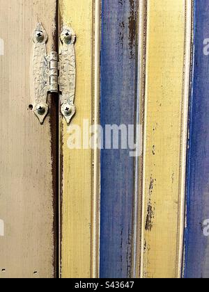 Door hinge and hardware on left with thick yellow and blue pastel striped wall. Stock Photo