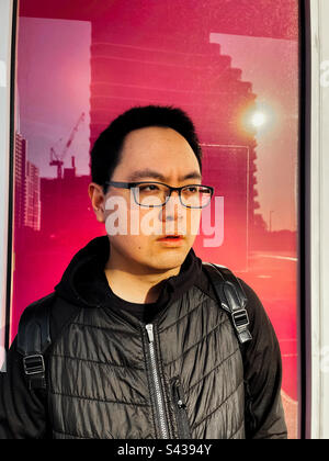 Portrait of young Asian man in eyeglasses standing against reflection of city buildings in pink glass door in Melbourne, Australia. Stock Photo