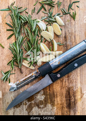 Chopping board with garlic and rosemary with knife and vegetable peeler Stock Photo