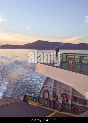 Man taking photos of a beautiful sunset on the back of a ferry boat in the Puget Sound, Washington State, USA. Stock Photo