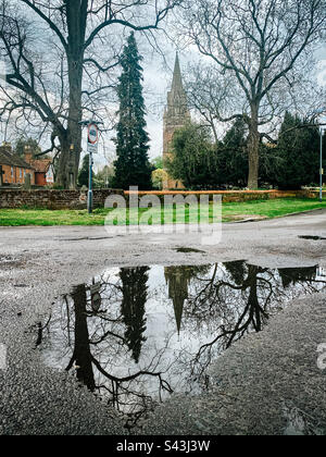 A puddle on the road as a result of April showers in front of St Michael’s Church in Tilehurst, Reading, UK Stock Photo