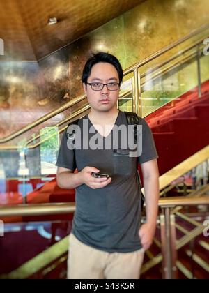 Young Asian man using hand phone against staircase and railings. Stock Photo