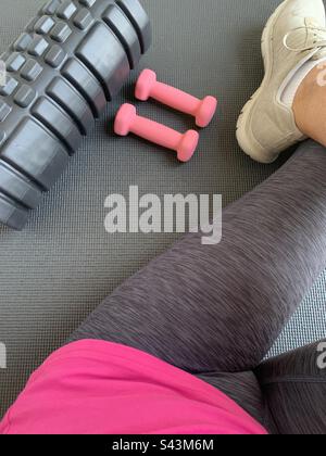 Closeup image of a lady about to begin a gym workout using a mat, a back roller and a pair of dumbbells Stock Photo