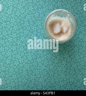 Closeup image of an empty glass of cappuccino coffee against a green floral background Stock Photo