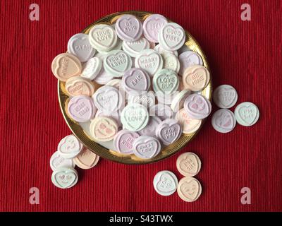 Love Hearts. Love Hearts in a white dish with a gold rim on a red background. Valentines Day. Candy. Stock Photo