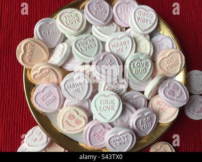 Love Hearts. Love Hearts in a white dish with a gold rim on a red background. Valentines Day. Candy. Stock Photo