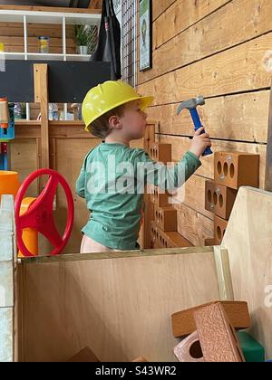 Educational young boy hammering a pretend brick wall wearing a yellow hats hat Stock Photo