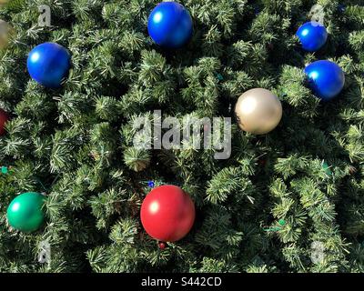 Detail of large red, blue, white and green ornaments on a giant artificial Christmas tree, outdoors in Southern California Stock Photo