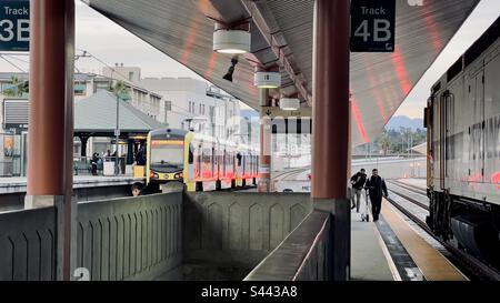 LOS ANGELES, CA, DEC 2022: two passengers approaching the side of a Metrolink train, using scooters on platform at Union Station in Downtown. LA Metro Gold Line train visible in background Stock Photo