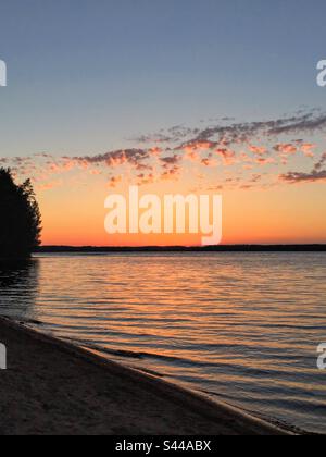 Side perspective view to the stunning magic dramatic sunset over the sea water surface with the sunlight reflection from the sand shore Stock Photo