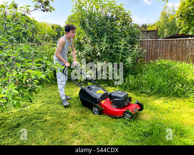 A teenage boy cutting a back lawn with a petrol lawnmower Stock Photo