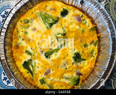 A healthy crustless quiche made with eggs, farmer’s cheese, ham and broccoli and topped with cheddar cheese before baking. Stock Photo