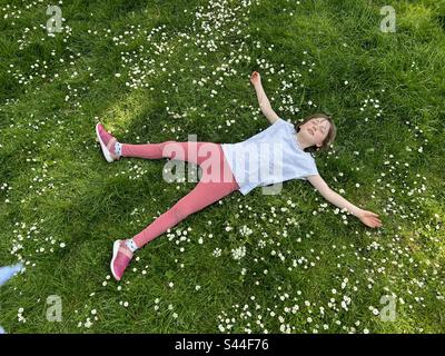 8 year old girl lying on the grass full of daisies Stock Photo