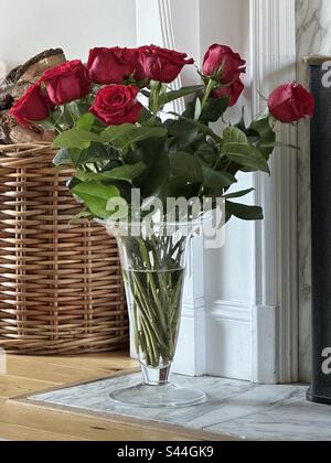 Bunch of red roses in a glass vase on the marble floor in front of a fireplace Stock Photo
