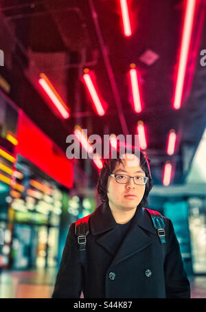 Portrait of young Asian man standing against multicolored neon lights in the city at night. Stock Photo
