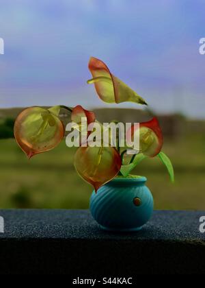 Red and yellow artificial flowers in blue pot with beautiful background Stock Photo