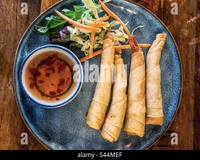 Directly above view of four crispy prawns encased in pastry wrappers together with fresh salad and chili dip on plate on table. Lumpia. Spring rolls. Stock Photo