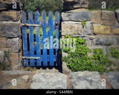 Old wooden gate with faded blue paint in a natural stone wall. Stock Photo