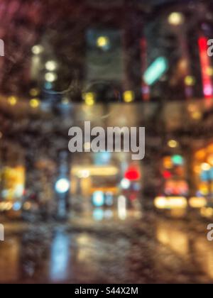 Abstract shot of city street and illuminated building exterior seen through wet car window on a rainy night. Defocused. Bokeh. Backgrounds Stock Photo