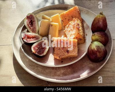 Close-up of fresh figs, whole and sliced, cheese and slices of rose chiffon cake on plates on table. Snack, dessert. Stock Photo