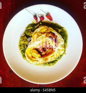 Fried eggs with bacon and three red hot chilli peppers on top of green chilaquiles in Queretaro, Mexico Stock Photo