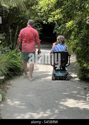 Man and elderly woman in mobility scooter explore lost gardens of Heligan, Cornwall, England in summer Stock Photo