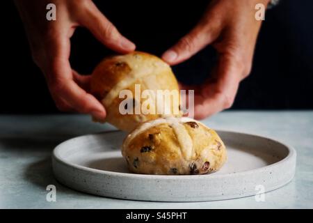 Woman’s hands placing hot cross buns on a plate Stock Photo