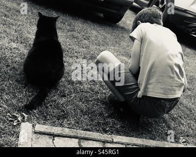 Black cat and boy child sitting on grass Stock Photo