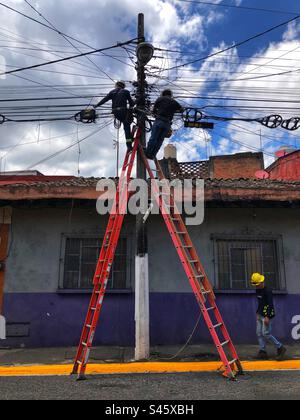 Two electricians staying on the stepladders doing cable work with another one on the ground, Xalapa, Mexico, 2022 Stock Photo