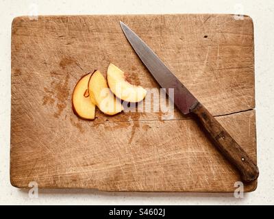 Three nectarine slices and kitchen knife on old wet wooden chopping board. Stock Photo