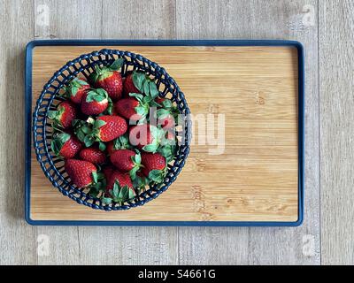 Directly above view of fresh, organic strawberries in black basket on wooden cutting board on wooden table with copy space. Stock Photo